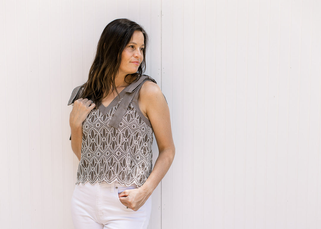 Model wearing a mocha sleeveless top with cream floral embroidery and a scalloped hem.