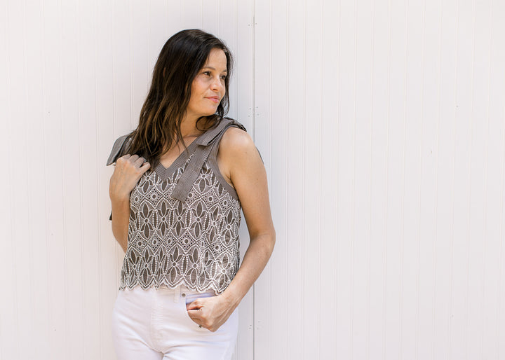 Model wearing a mocha sleeveless top with cream floral embroidery and a scalloped hem.
