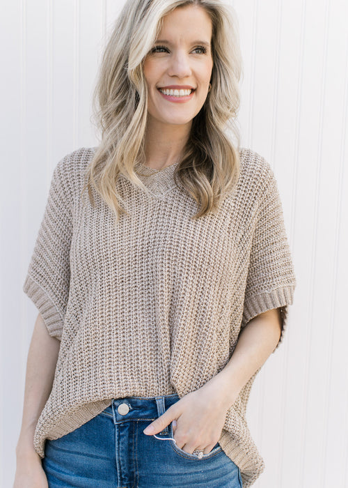 Model wearing a taupe knit sweater with extended shoulder short sleeves and a v-neck.