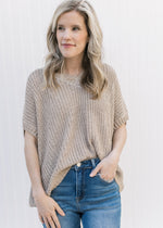Model wearing jeans and a taupe knit sweater with extended shoulder short sleeves and a v-neck.