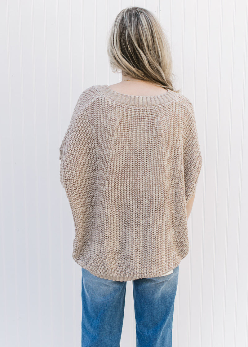 Back view of Model wearing a taupe knit sweater with extended shoulder short sleeves and a v-neck.