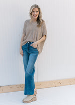 Model wearing jeans and mules with a taupe knit sweater with short sleeves and a v-neck.