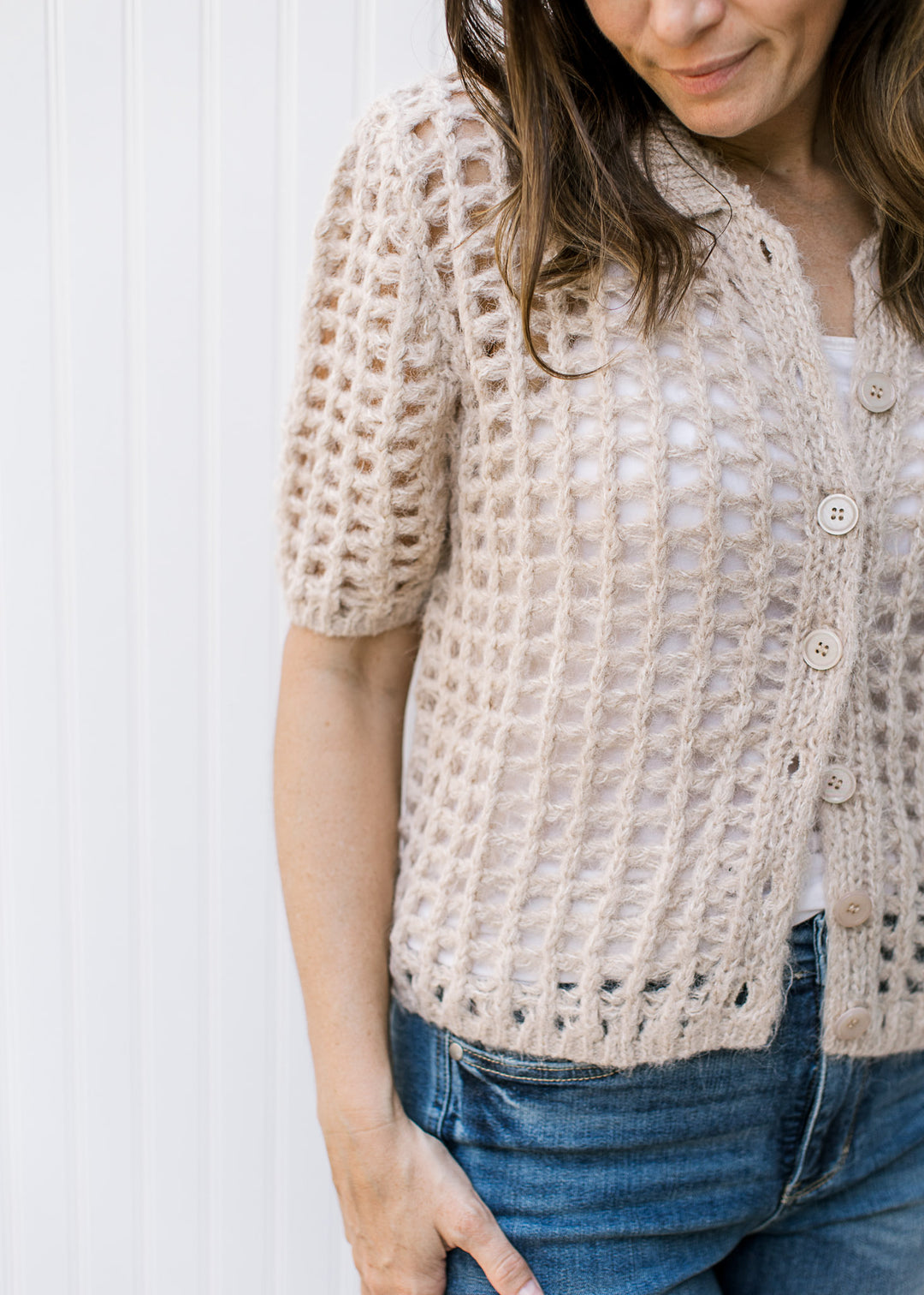 Model wearing a oatmeal colored, open crochet cardigan with short sleeves and button front. 