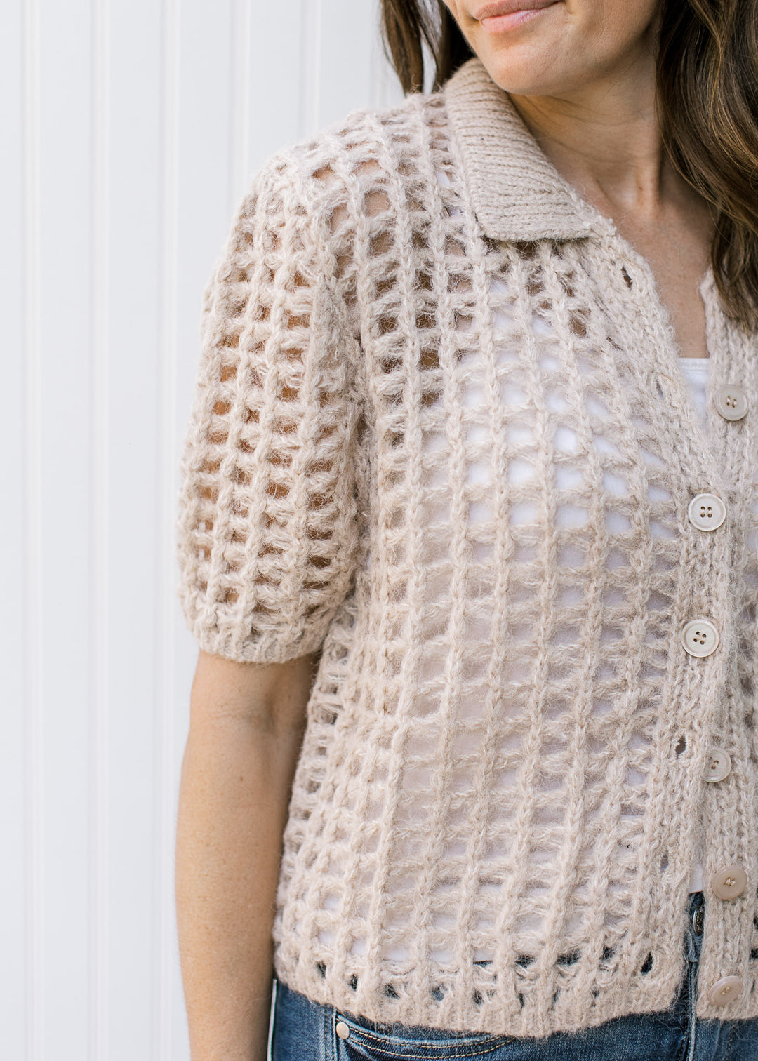 Close up of Model wearing a oatmeal colored, open crochet cardigan with a button front. 