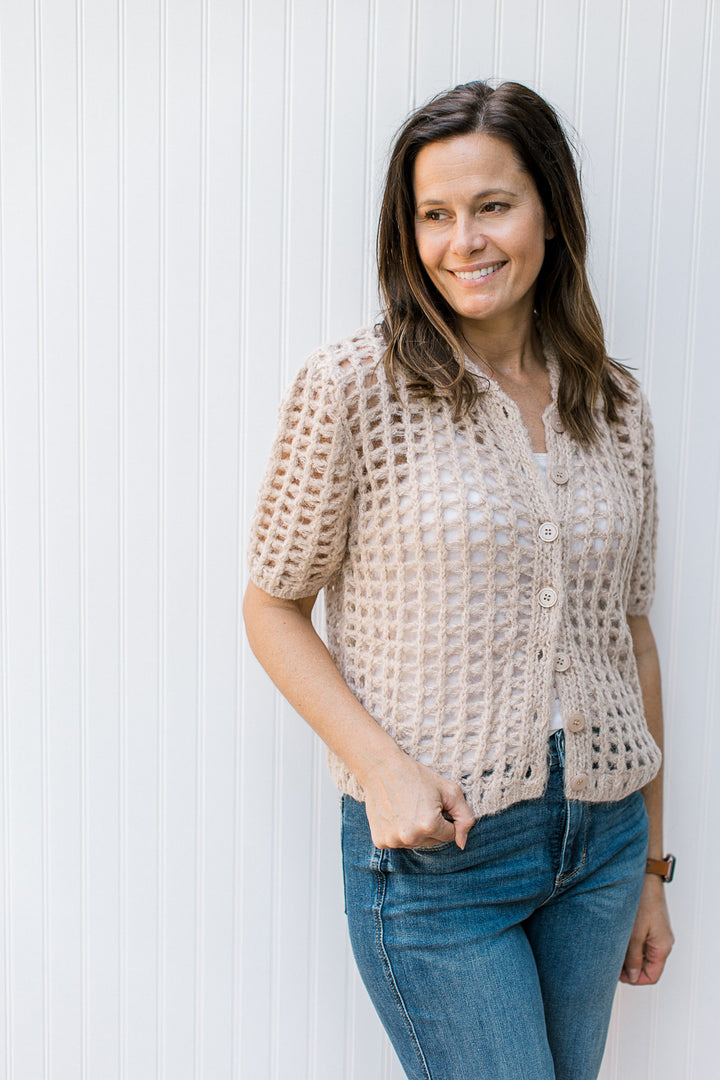Model wearing a oatmeal colored, open crochet cardigan with flap collar and button front. 