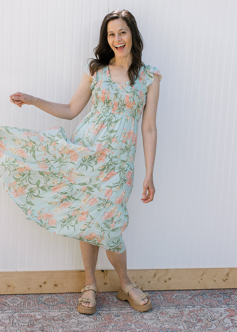 Model wearing a baby blue midi with peach floral, a smocked bodice and flutter capped sleeves.