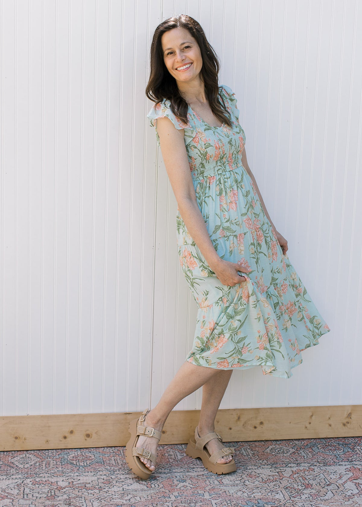 Model wearing a v-neck baby blue midi with peach floral, a smocked bodice and capped sleeves.