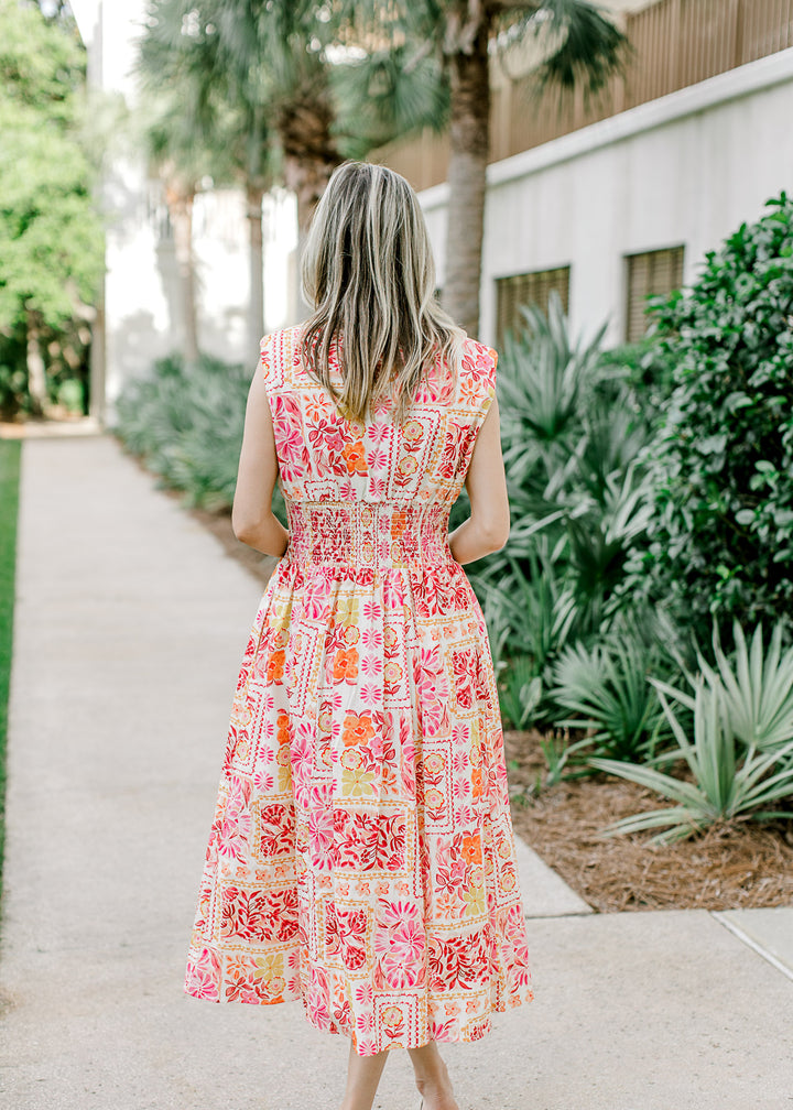 Back view of Model wearing an off white midi with bright floral, v-neck and shoulder pads.