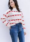 Model wearing a cream ribbed sweater with a striped heart pattern, mock neck and long sleeves. 