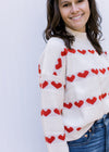 Close up of striped red heart pattern on a cream ribbed sweater with long sleeves and a mocked neck.