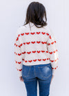 Back view of Model wearing a cream sweater with a heart pattern, mock neck and long sleeves. 