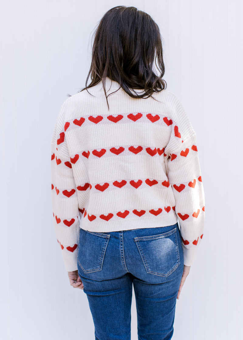 Back view of Model wearing a cream sweater with a heart pattern, mock neck and long sleeves. 