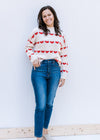 Model wearing jeans with a cream sweater with a striped heart pattern, mock neck and long sleeves. 
