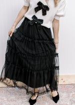 Model wearing a black tule midi with tiers an elastic waist and a mesh overlay. 