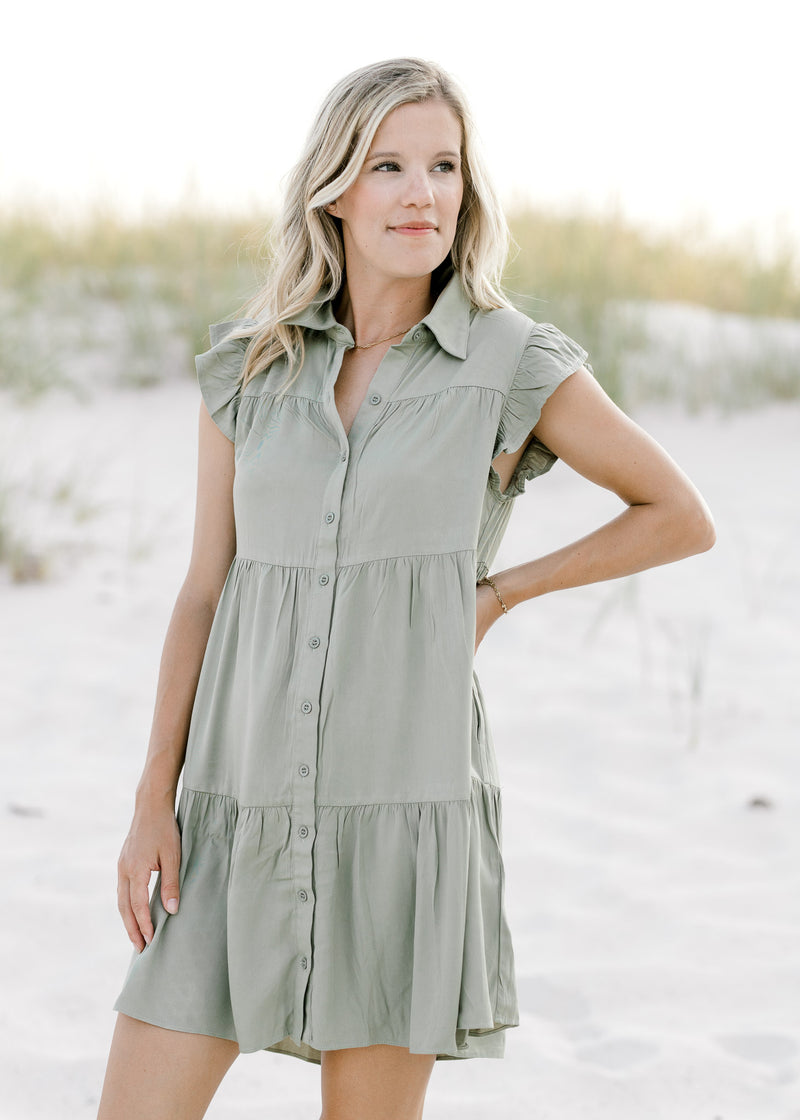 Model wearing a tiered, above the knee, olive dress with flutter cap sleeves and button closure. 