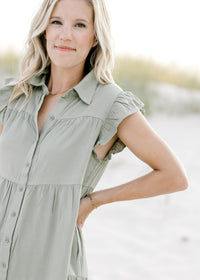 Close up view of button closure and cap short sleeves on an olive above the knee dress. 
