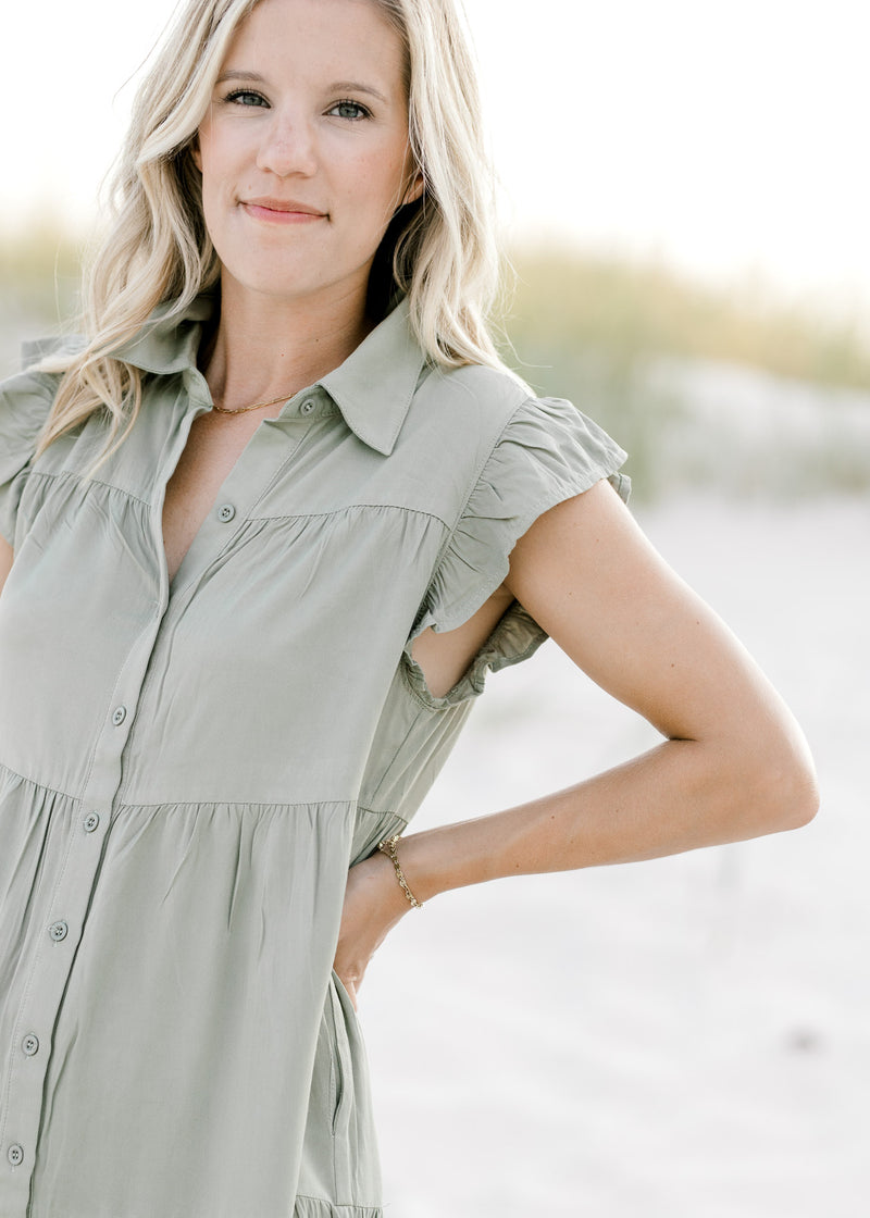Close up view of button closure and cap short sleeves on an olive above the knee dress. 