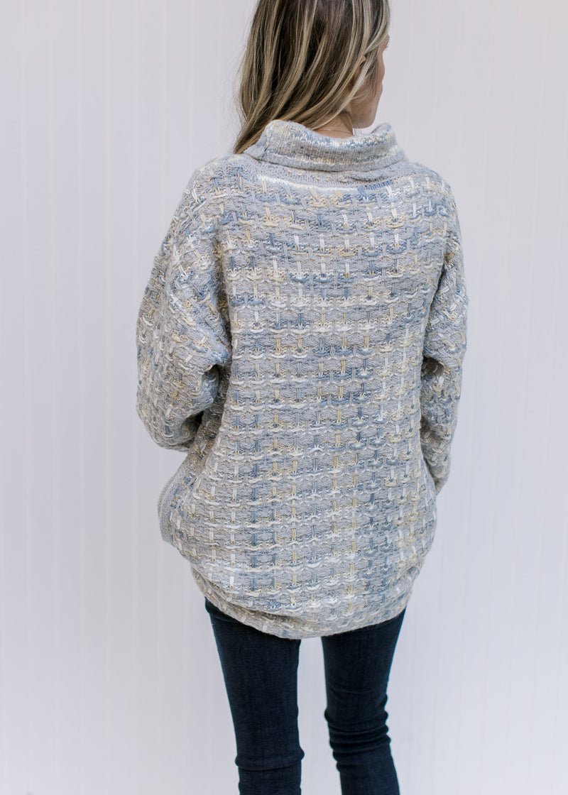 Back view of Model wearing a tweed sweater with a turtleneck, long sleeves and pockets. 