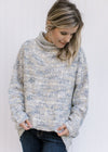 Model wearing a long sleeve gray, cream and mustard tweed sweater with a turtleneck and pockets. 