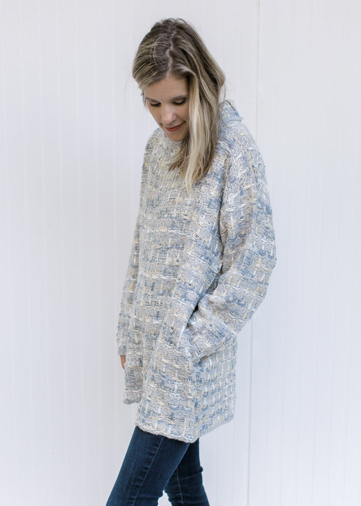 Side view of Model wearing a tweed sweater with a turtleneck, long sleeves and pockets. 