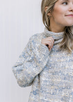 Close up of the turtleneck on a gray, cream and mustard tweed sweater with long sleeves. 