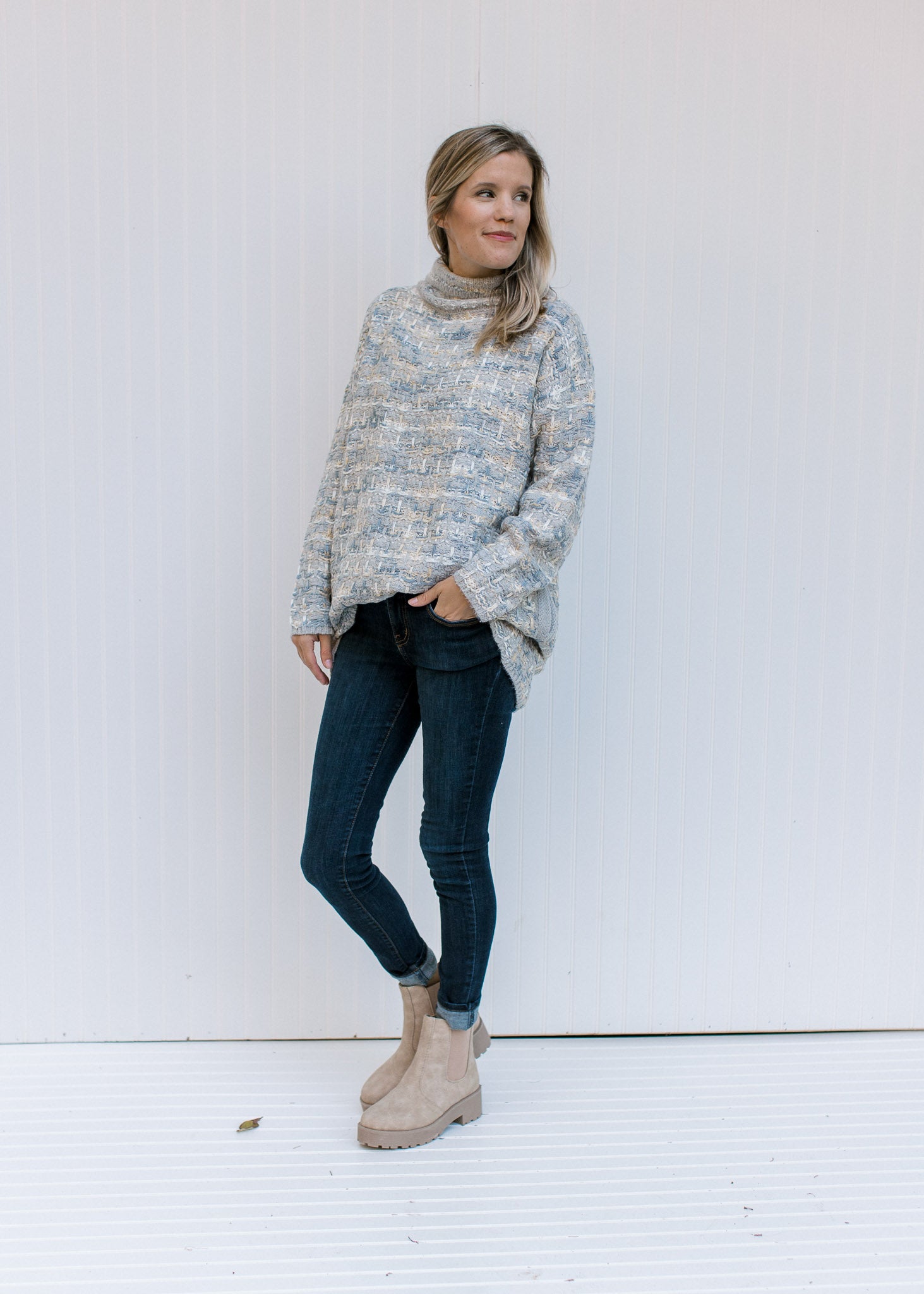 Model wearing jeans and booties with a tweed sweater with a turtleneck, long sleeves and pockets. 