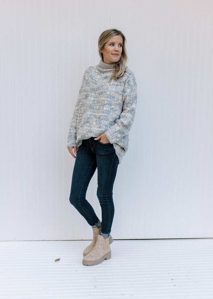 Model wearing jeans and booties with a tweed sweater with a turtleneck, long sleeves and pockets. 