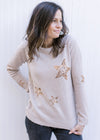 Model wearing a taupe knit sweater with gold sequin stars, long sleeves and a round neck.