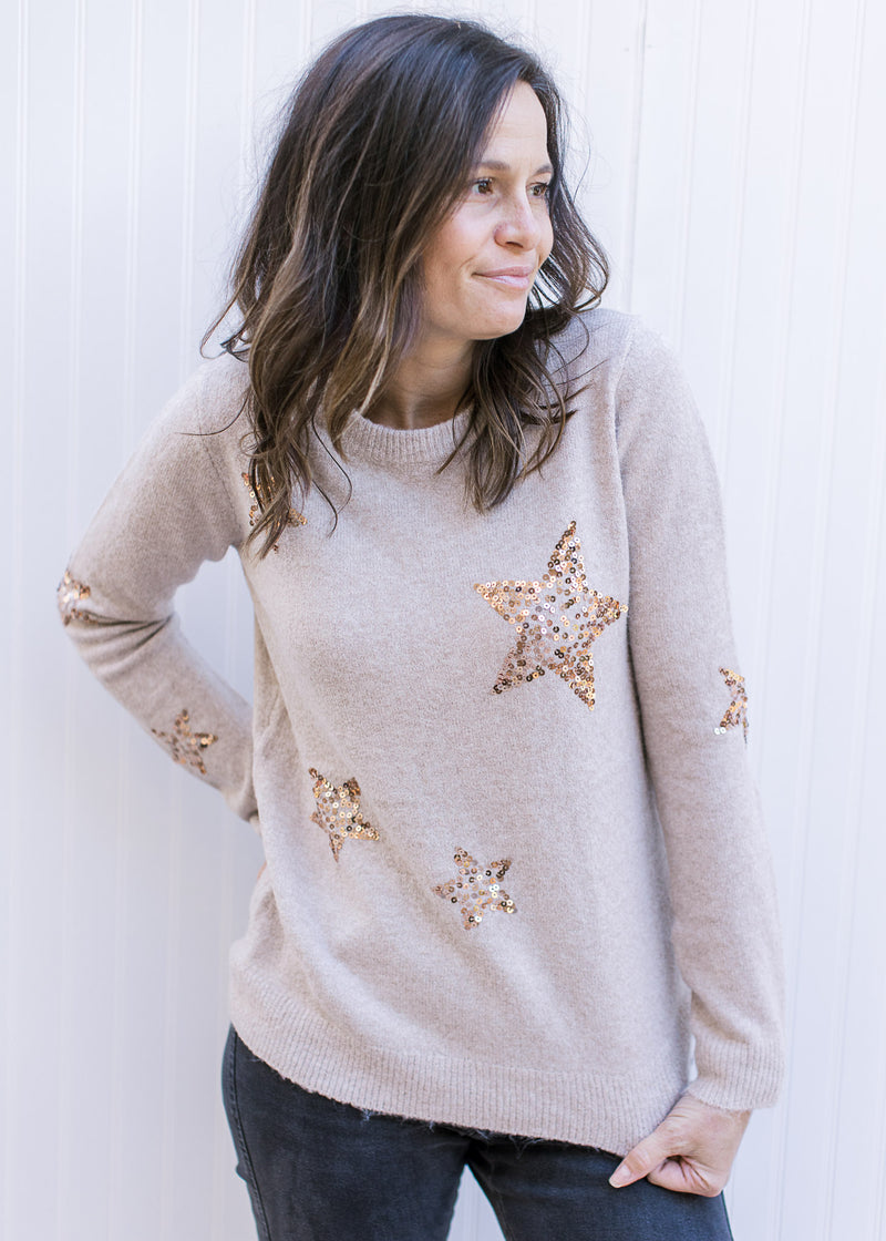 Model wearing a taupe knit sweater with gold sequin stars, long sleeves and a round neck.