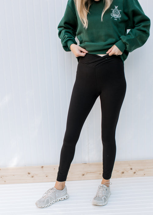 Model wearing a sweatshirt and sneakers with black leggings with a v-front. 
