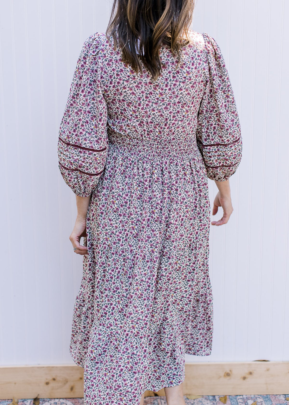 Back view of Model wearing a cream dress with plum ditsy flowers, 3/4 sleeve and a smocked waist.