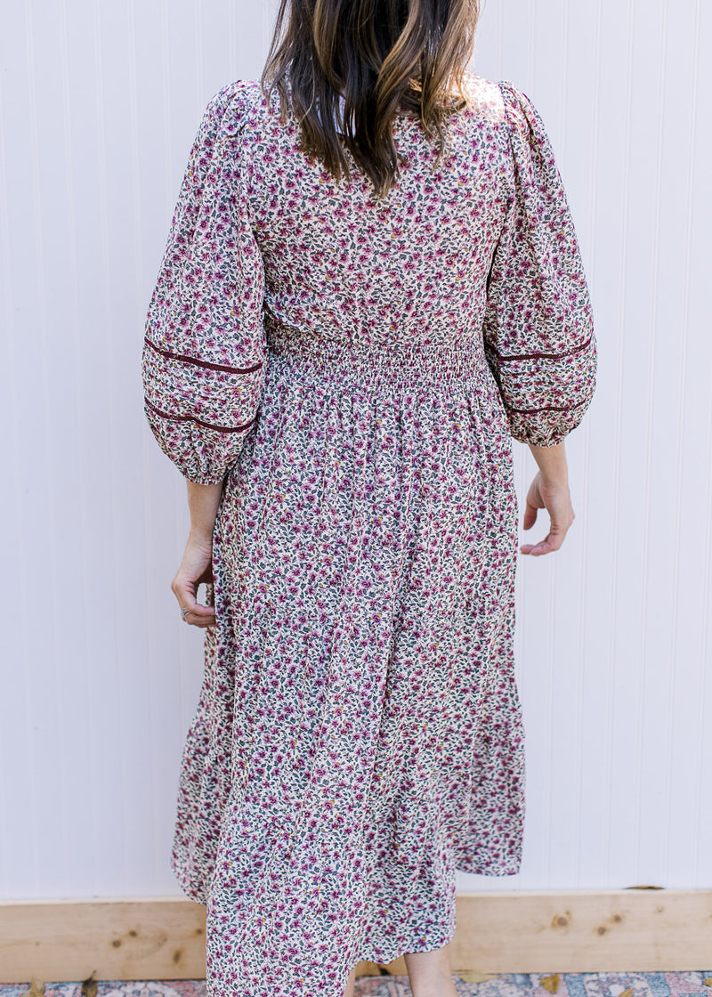 Back view of Model wearing a cream dress with plum ditsy flowers, 3/4 sleeve and a smocked waist.