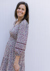 Model wearing a cream v-neck dress with plum ditsy flowers, 3/4 sleeve and a smocked waist. 