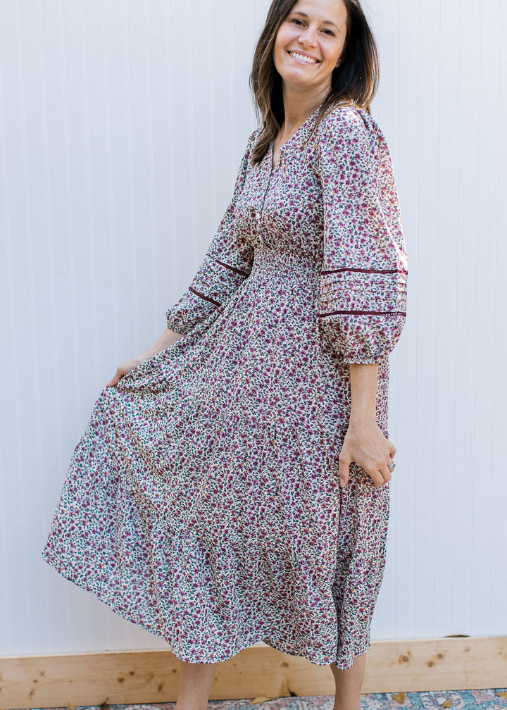 Model wearing a cream dress with plum ditsy flowers, 3/4 sleeve, smocked waist and v-neck. 