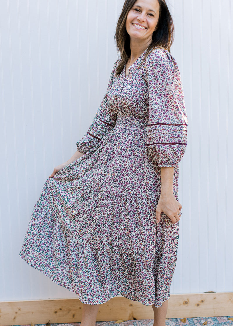 Model wearing a cream dress with plum ditsy flowers, 3/4 sleeve, smocked waist and v-neck. 