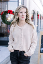 Model wearing a creamy knit button front cardigan with long sleeves and a slightly  cropped fit.