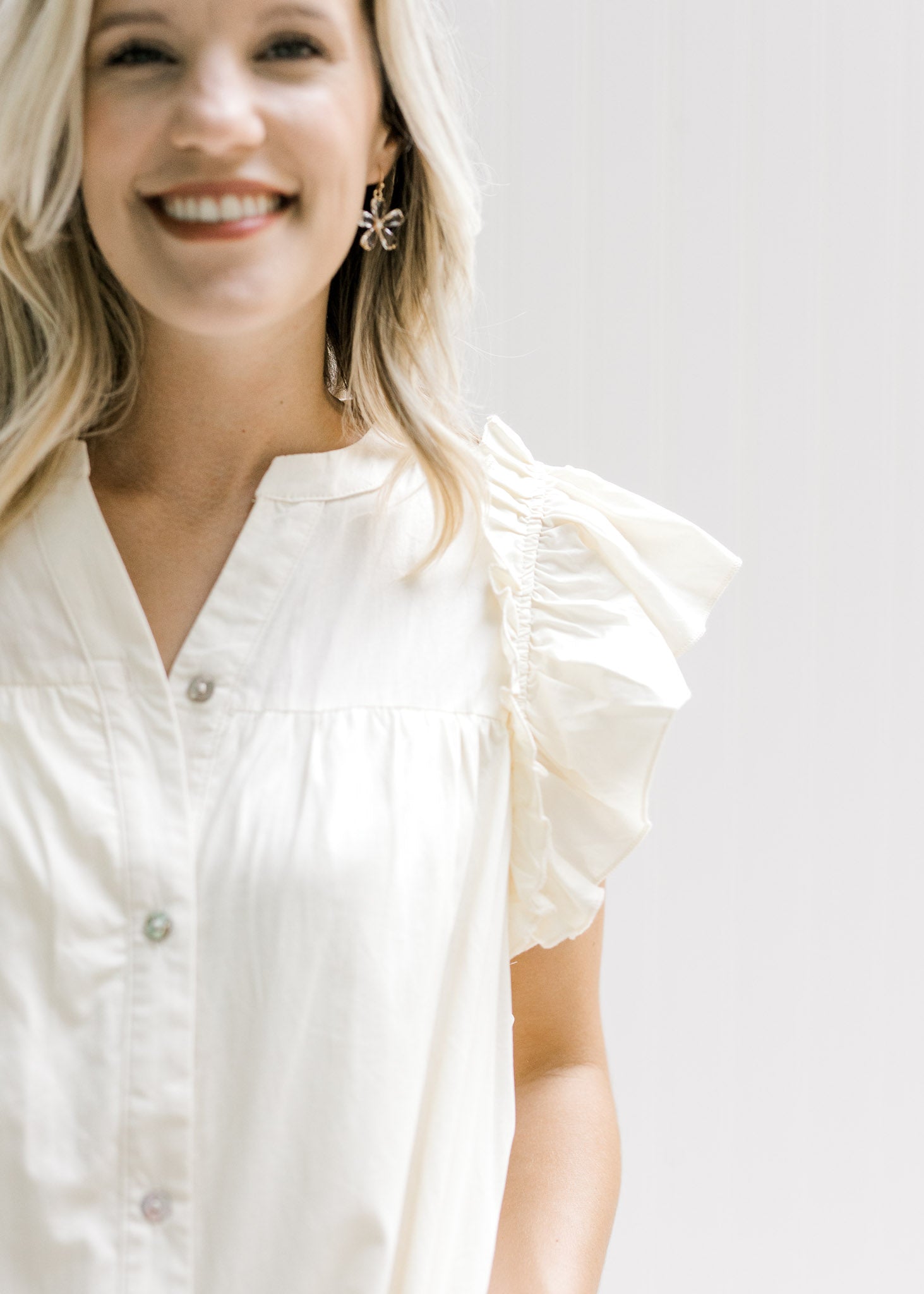 Close up view of buttons and ruffle capped sleeve on a v-neck cream above the knee dress. 