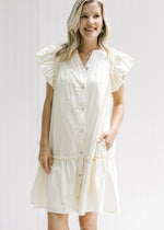 Model wearing a cream dress with pockets, ruffle cap sleeve and button down front. 