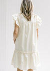Back view of Model wearing a cream dress with pockets, ruffle cap sleeve and button down front. 