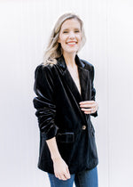 Model wearing a black velvet blazer, composed of polyester with long sleeves and a ruched detail.