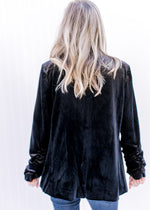 Back view of Model wearing a black velvet blazer with long sleeves and a ruched detail. 
