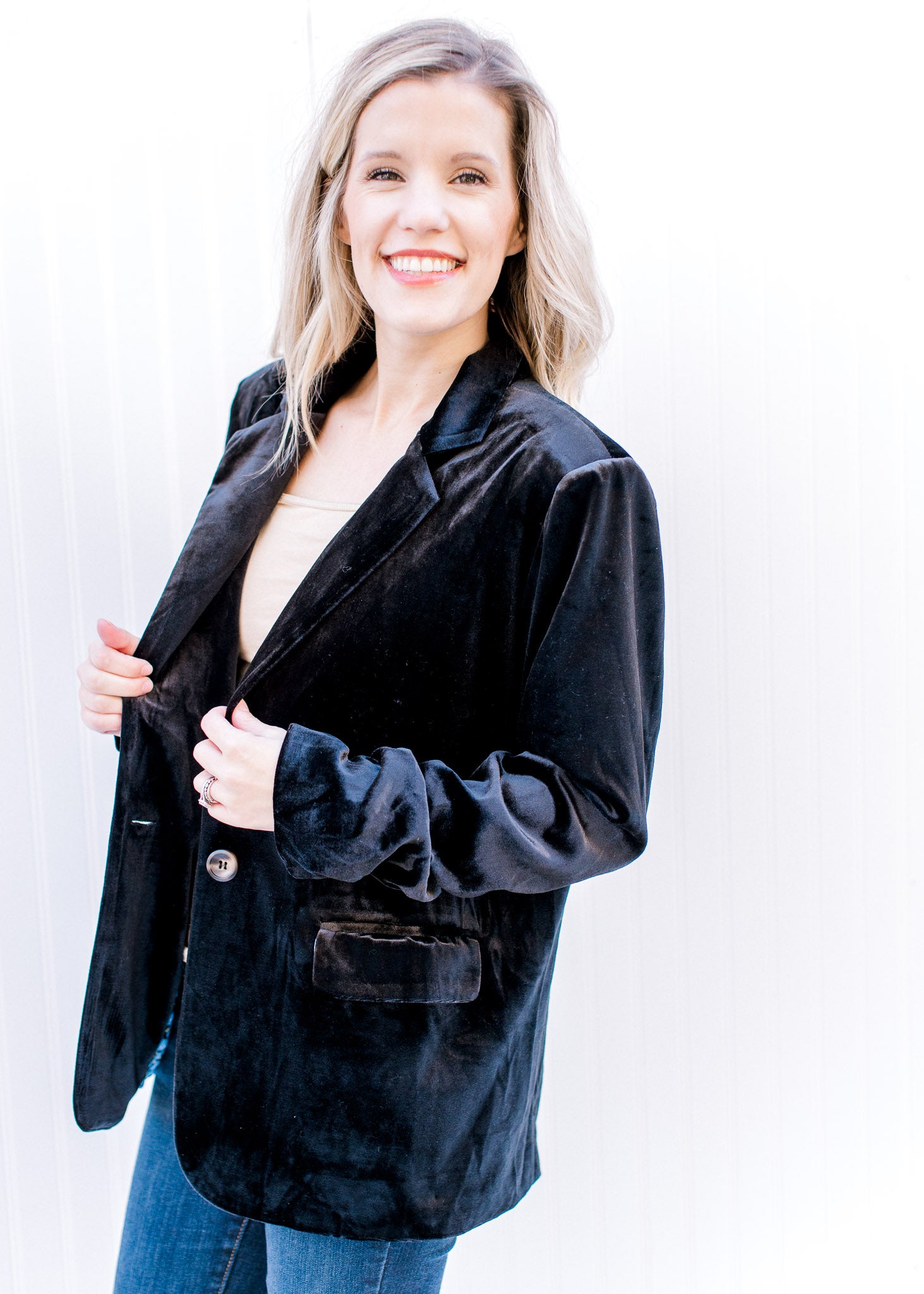 Model wearing jeans with a black velvet blazer with faux flap pockets and long sleeves. 