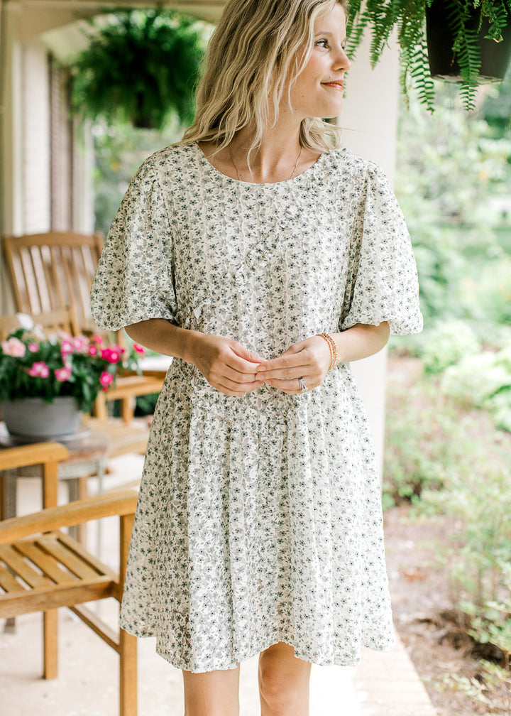 Model wearing a cream above the knee dress with green floral, cross ruffle and short bubble sleeves.