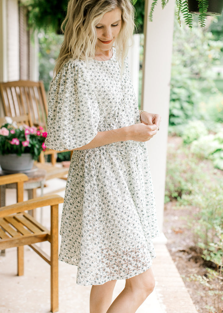 Model wearing a cream dress with green floral, round neck, cross ruffle and short bubble sleeves.