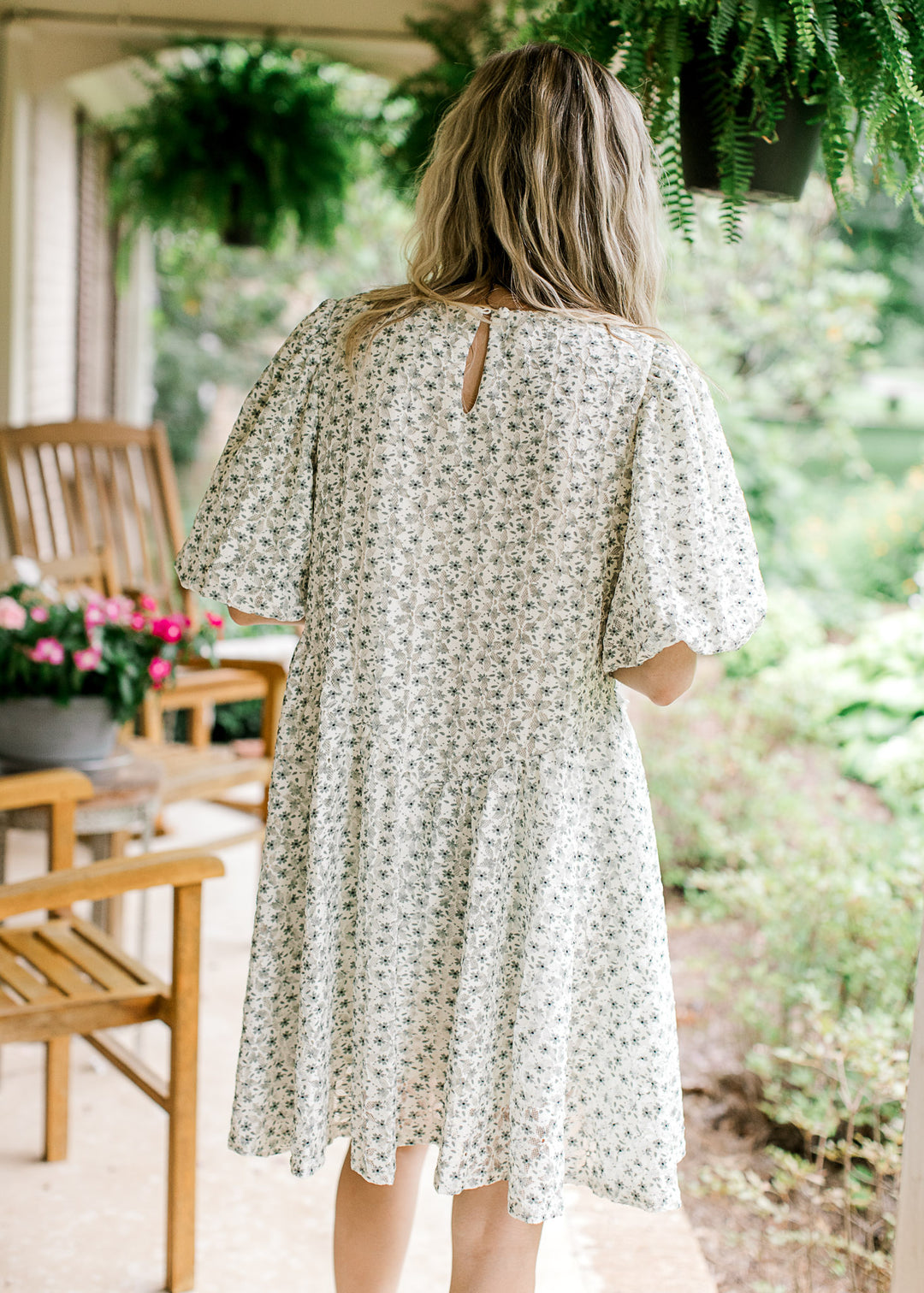 Back view of Model wearing a cream dress with green floral, cross ruffle design and keyhole closure.