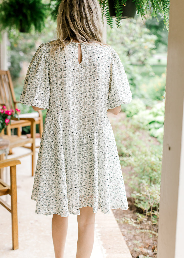 Back view of model wearing a cream dress with green floral, cross ruffle and short bubble sleeves.