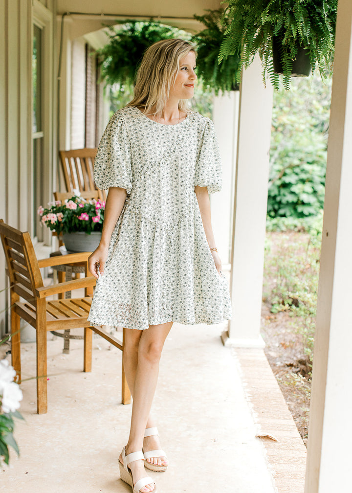 Model wearing heals and a cream dress with green floral, cross ruffle and short bubble sleeves.