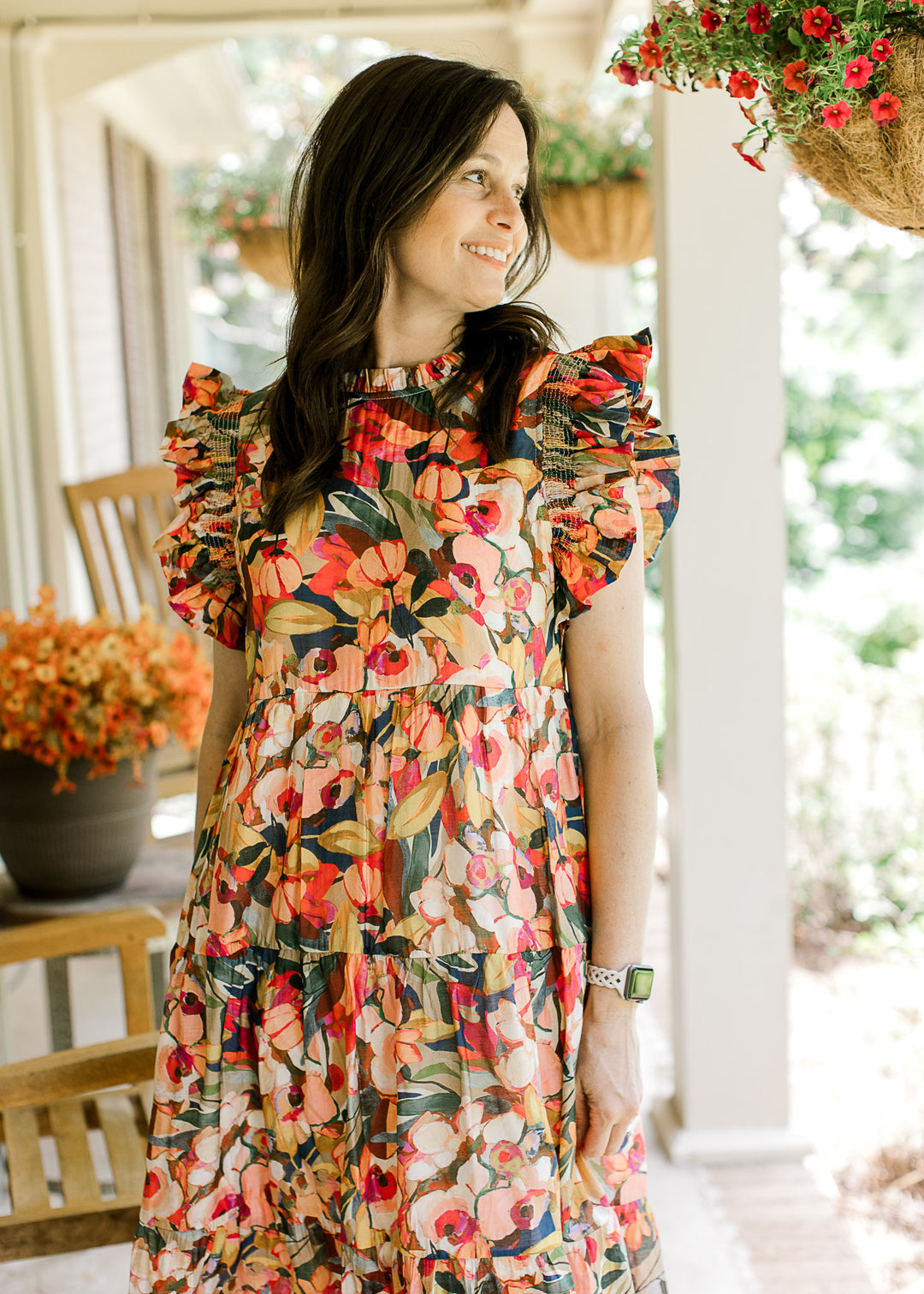 Model wearing a bright floral midi with cap sleeves, round neck with ruffle and a tiered skirt.