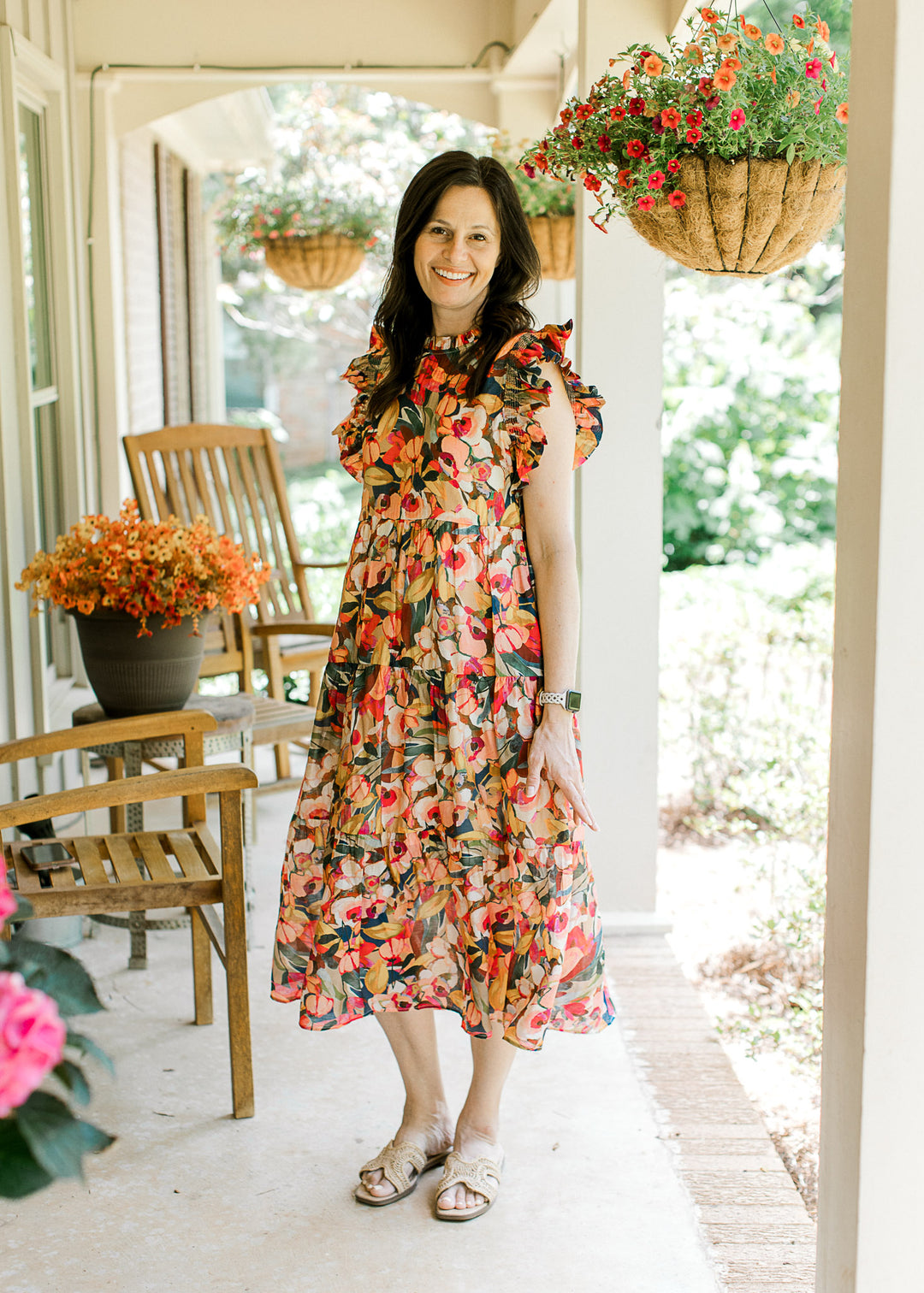 Model wearing flats and a bright floral midi with cap sleeves, round neck and a tiered skirt.