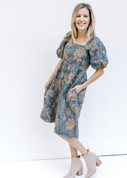 Model wearing booties and a blue midi dress with floral stitching, a square neck and short sleeves.